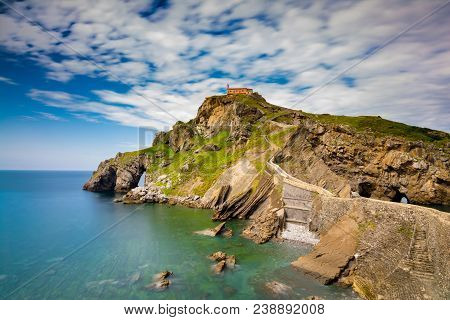 Brown Building Above Clif Near Body Of Water. Gaztelugatxe.