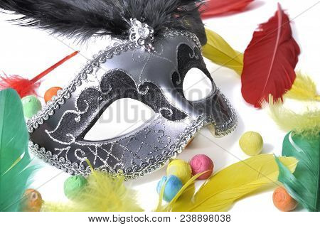 Dark Beautiful Carnival Mask Among Colorful Feather And Paper Balls On White Backgroung