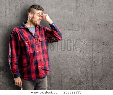 Young handsome man with sleepy expression, being overworked and tired, rubbes nose because of weariness