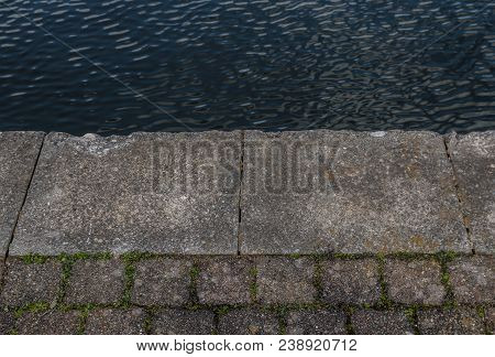 The Edge Of The Paved Towpath As It Meets The Waters Of The Canal