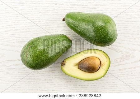 Two Green Smooth Avocado And One Section Half With A Seed Table Top Isolated On Grey Wood Background