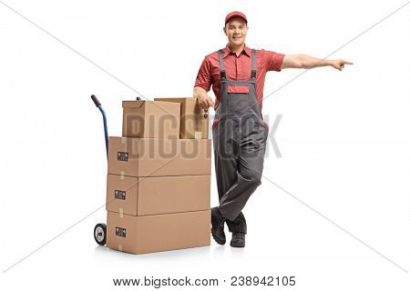 Full length portrait of a mover leaning on a hand truck with a stack of boxes and pointing isolated on white background