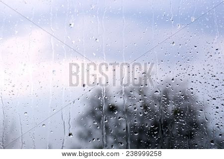 Raindrops On Glass, Clouds And Tree In The Background. Weather Forecast. Spring Rainy Background.