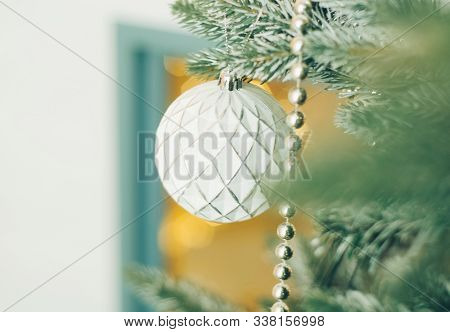 White Christmas Ball Toy And A Silver Beads On The Snow Branch Of A Green Tree. Festive Yellow Light