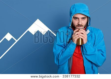 Serious Sad Bearded Man Basking Hands With Thermo Mug Of Tea Or Coffee, Dresses Blue Coat And Red Sh