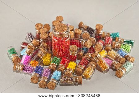 Red, Yellow, Blue, Green, Purple, Pink And Orange Beads In Glass Jars On A Gray Background. Beads In