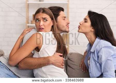 Jealousy And Infidelity. Girl Hugging Cheating Boyfriend While He Kisses Her Friend Sitting Together