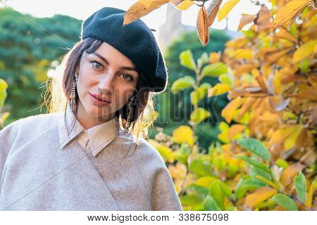 Attarctive Young Woman With Natural Makeup Dressed In Black Beret And Grey Dress Stands Among Autumn
