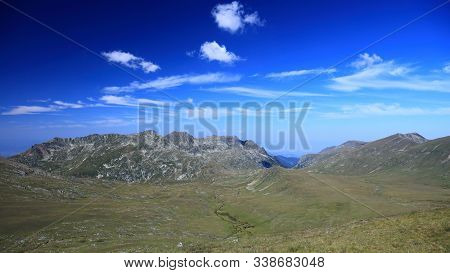 High Attitude Green Tableland With River Flowing Through And Mighty Mountains In The Background Duri
