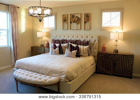 Queen Sized Bed With A Footrest And A Chandelier Hanging From The Ceiling Taken Inside A Contemporar