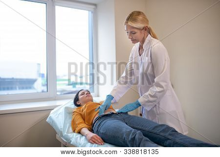 Blond Doctor Wearing Sterile Gloves Palping Patients Stomach