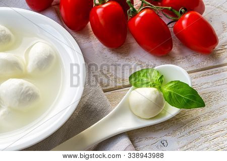 Close-up Of A Mini Mozzarella Cheese Ball And Basil In A Wite Porcelain Spoon Near Branch Of Red Che