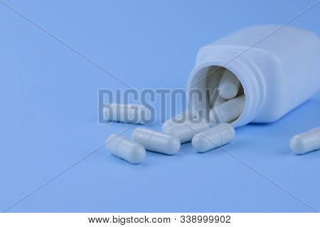 White Capsules Of Medicines On A Blue Background. Scattered Capsules From A Container On A Blue Back