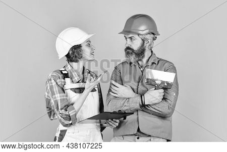 Two Parters. Couple Looking At A Blueprint. Woman And Man Wear Safety Hardhat. Family Standing Insid