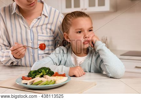 Mother Feeding Her Daughter In Kitchen, Closeup. Little Girl Refusing To Eat Dinner
