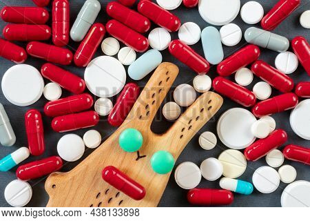 Wooden Rabbit With Green Pill Eyes Against The Background Of Many Pills, Pills And Vitamins. Concept