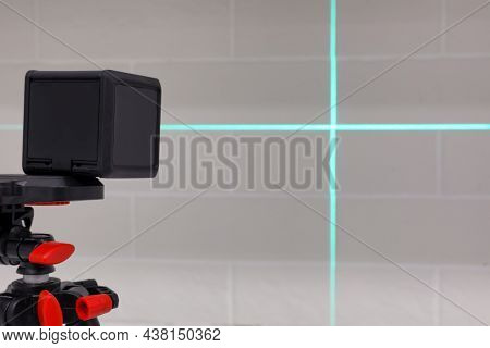 Cross Line Laser Level On Tripod In Front Of White Brick Wall