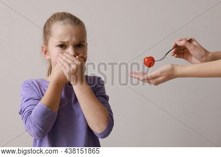 Cute Little Girl Covering Mouth And Refusing To Eat Tomato On Grey Background