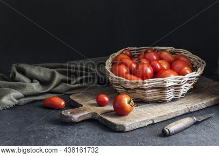 Fresh Red Tomatoes In Whicker Basket On Black Background. Copy Space