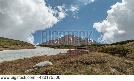 Mount Oshten Against A Blue Sky With Cumulus White Clouds. The Glade Is Partially Covered With Snow.