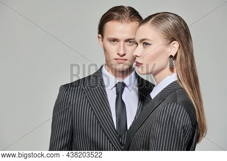 Stylish couple of young people man and woman in elegant striped pantsuits. Studio portrait on a gray background. Impeccable look. Fashionable business style.