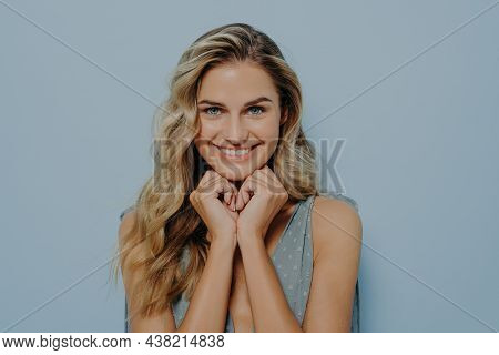 Dreamy Young Blonde Woman In Blue Dress With Hands Pressed Together Under Chin, Rejoicing After Hear