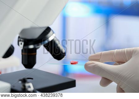 Scientist Holding Microscope Slide With Sample Of Red Liquid In Laboratory, Closeup