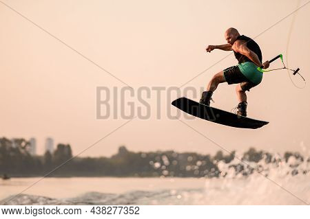 Great View Of Active Muscular Man Making Trick And Jump With Wakeboard On Sky Background.