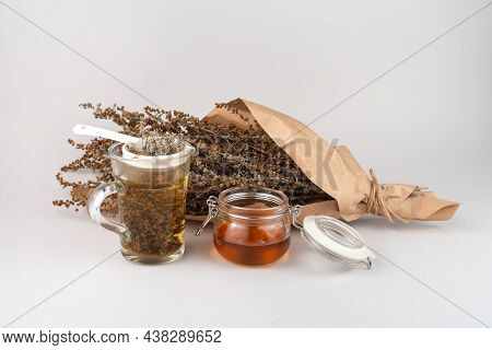 Glass Of Herb Tea, Tea Strainer, Honey And Wormwood Twigs Wrapped In Brown Paper.