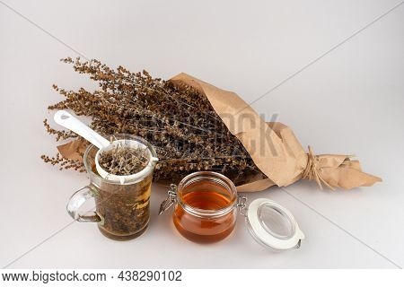 Glass Of Herb Tea, Tea Strainer, Honey And Wormwood Twigs Wrapped In Brown Paper.