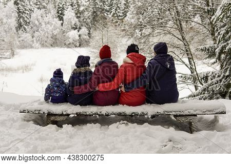 A Large Family Sit On A Bench In The Winter Forest