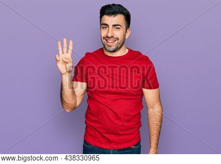 Hispanic man with beard wearing casual red t shirt showing and pointing up with fingers number three while smiling confident and happy. 