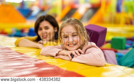 Pretty girls family together on colorful trampoline at playground park smiling. Beautiful kid daughter and her mother happy during active entertaiments indoor