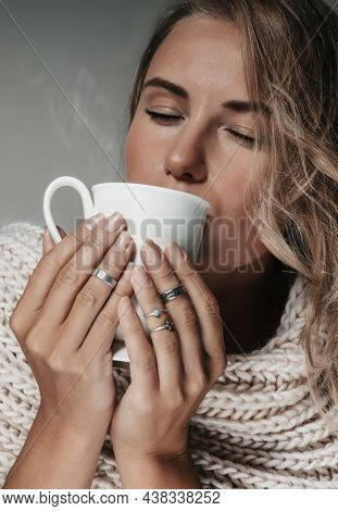 Closeup Portrait of a Beautiful Blond Woman Wearing Big Knitted Scarf Holding Cup of Hot Hearbal Tea. Fashion Look.