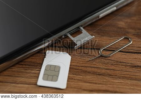 Sim Card, Mobile Phone And Ejector Tool On Wooden Table, Closeup