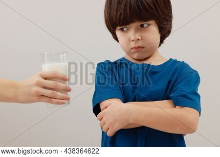 Cute Little Boy Refusing To Drink Milk On Grey Background
