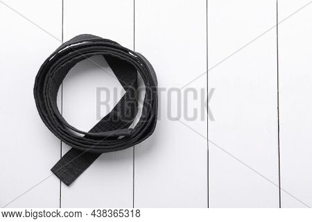 Rolled Black Belt On White Wooden Background, Top View With Space For Text. Oriental Martial Arts