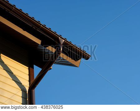 A Roof With A Gutter On A House Against A Blue Sky Background. Close-up
