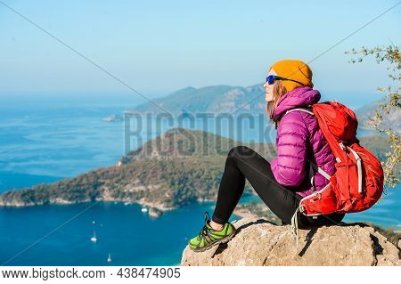 Young Woman Hiker In Bright Clothes Using Digital Tablet Sit At Seaside Cliff Edge And Enjoy The Vie