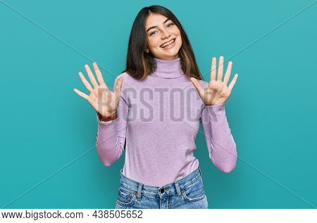 Young beautiful teen girl wearing turtleneck sweater showing and pointing up with fingers number ten while smiling confident and happy. 