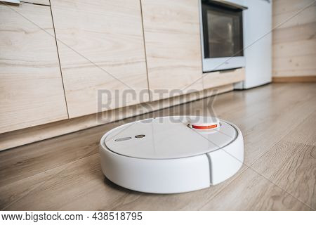 White Robotic Vacuum Cleaner Cleaning Wooden Floor In Modern Kitchen
