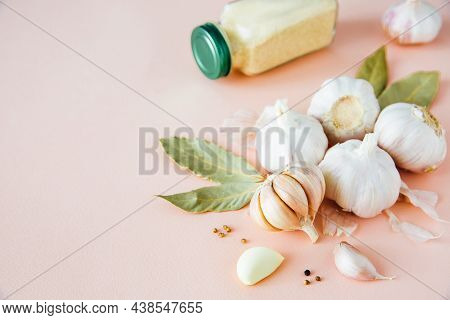 Garlic Bulbs On A Pink Background With Spices, Dried Garlic, Pepper And Bay Leaf. Spices And Condime