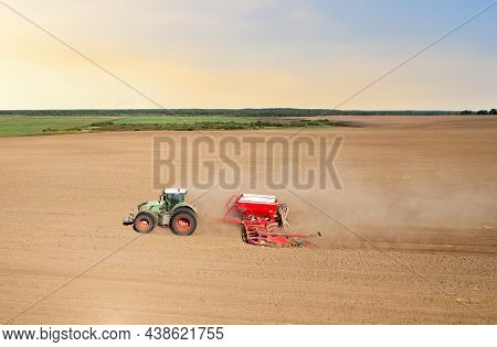 Agricultural Tractor Sowing Seed Onto At Field. Farming And Seeding Concept. Seeds Sowing In Farmers