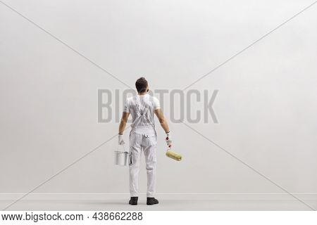 Rear view shot of a painter in front of a wall holding a bucket ana a paint roller isolated on white background