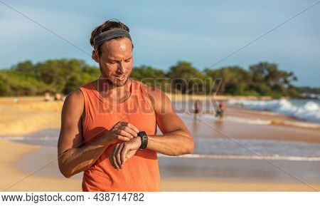 Running man athlete using smartwatch fitness app on wearable tech device smart sports watch training on beach. Runner working out sweating on summer day banner.