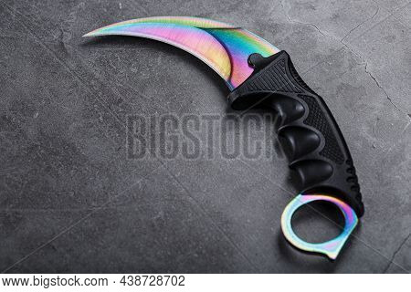 Kerambit Dagger With A Rainbow-colored Blade On A Dark Textured Background.