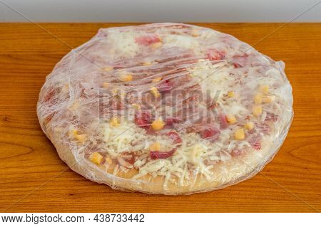 Frozen Pizza In Foil With Pepperoni On Wooden Table.