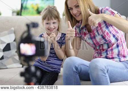 Portrait Of Mother And Daughter Showing Thumbsup On Video, Videocamera Set On Tripod. Little Girl An