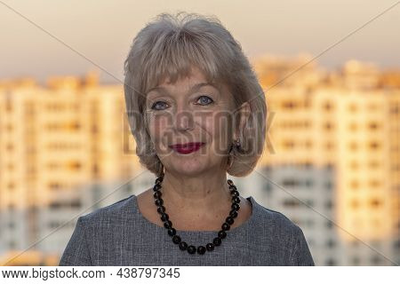 Portrait Of An Elderly Beautiful Smiling Woman 60-65 Years Old With Short Dyed Hair Against A Blurry