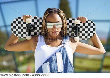 Black Female Dressed Casual, Looking At Camera With Modern Sunglasses And An Skateboard.